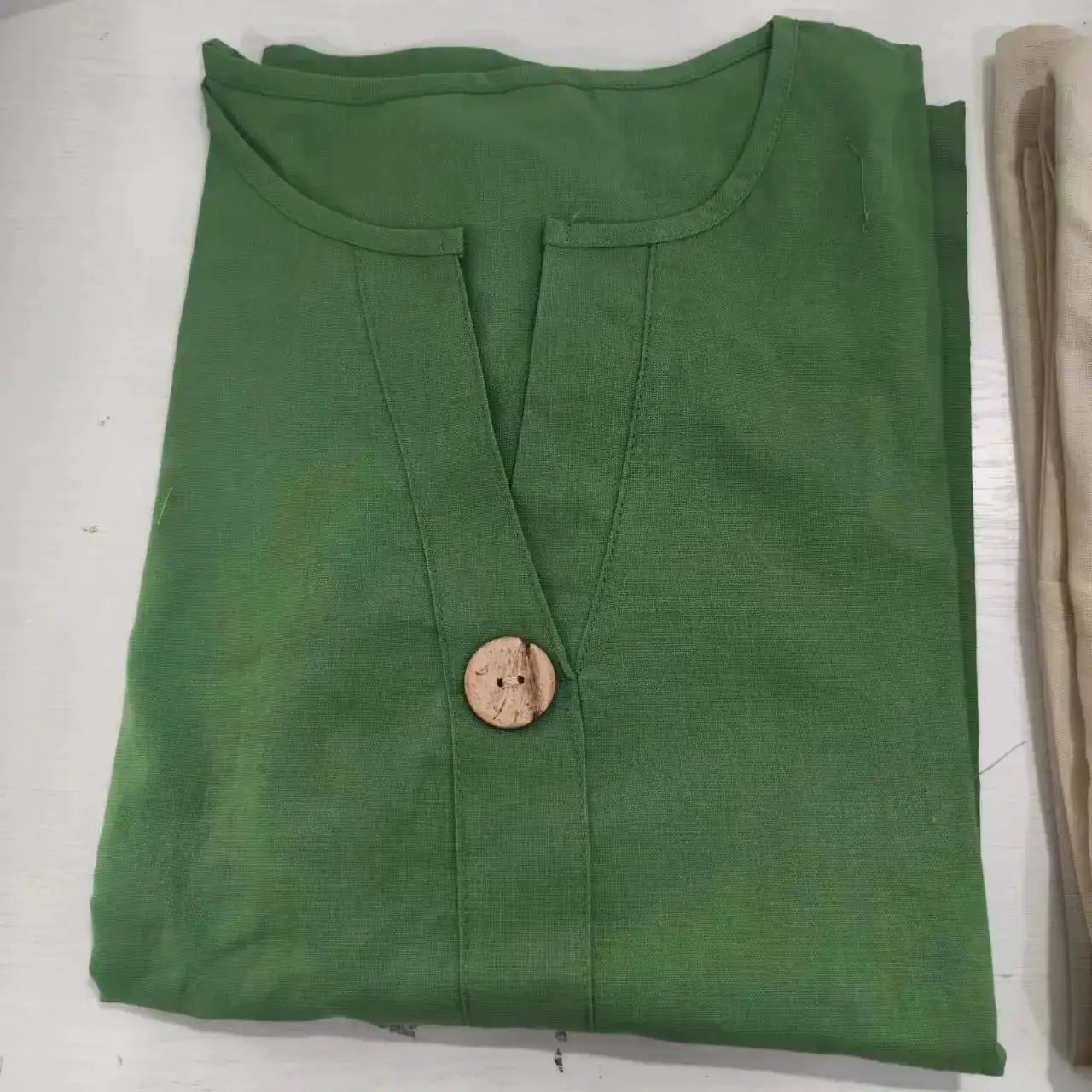 Green cotton-linen blouse with V-neck placket and single wooden button.