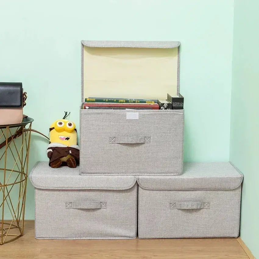 Washable cotton-linen folding storage boxes; three gray fabric bins with lids, top bin open with books.