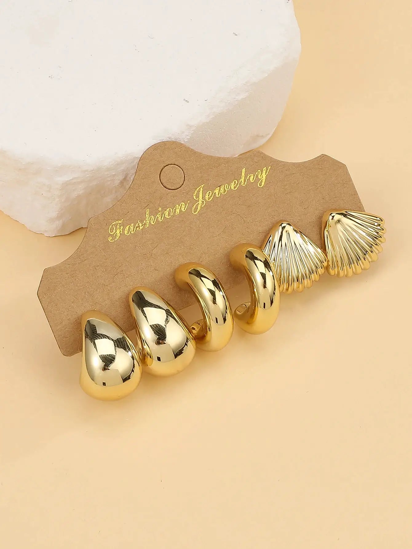 Gold-tone fashion earrings set with curved C-shape hoops and ribbed seashell drops on brown display card