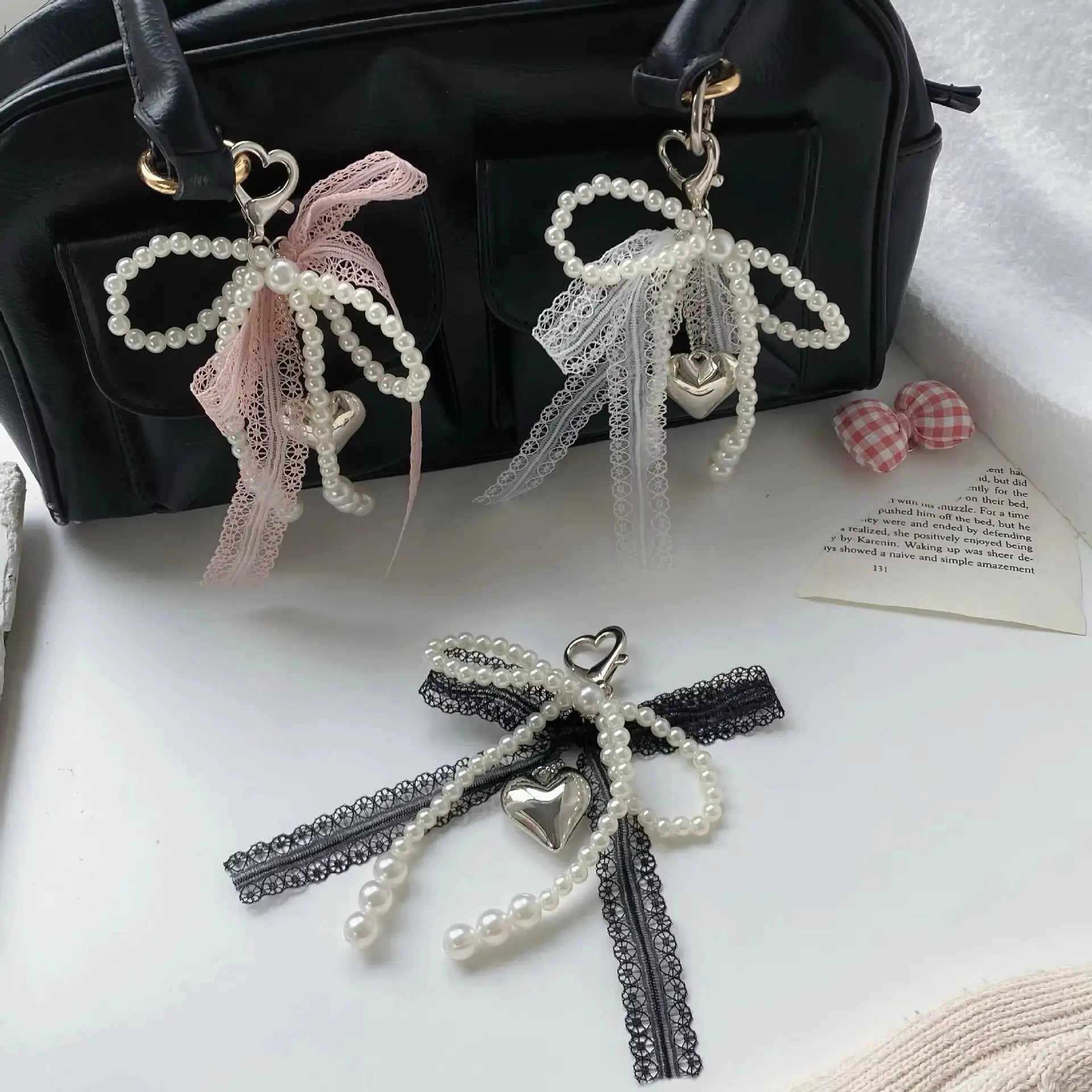 Two Y2K imitation pearl lace bowknot keychains with heart charms on a black handbag, pink and white lace