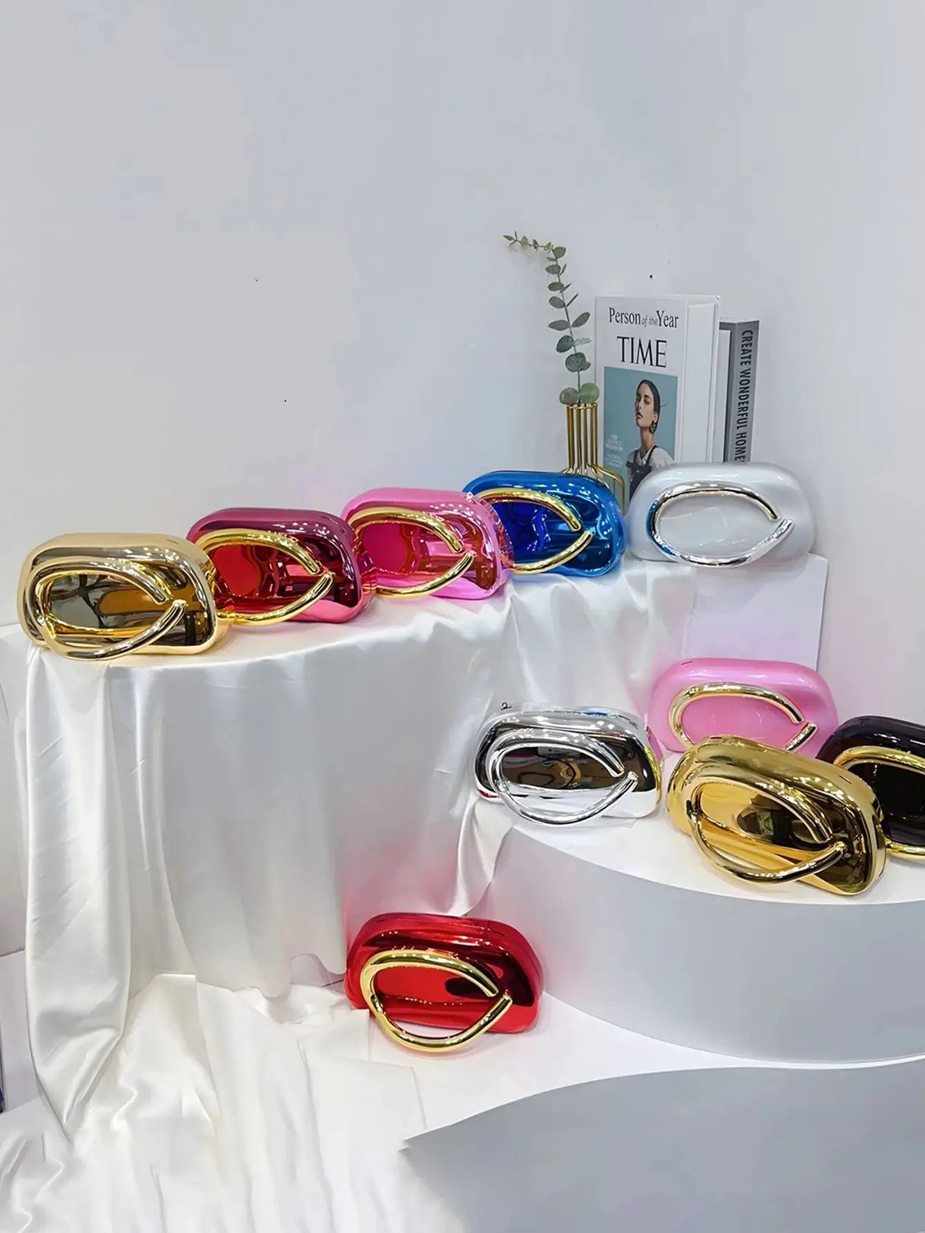 Group of acrylic box crossbody bags in metallic colors with gold oval handles, displayed on white draped surface
