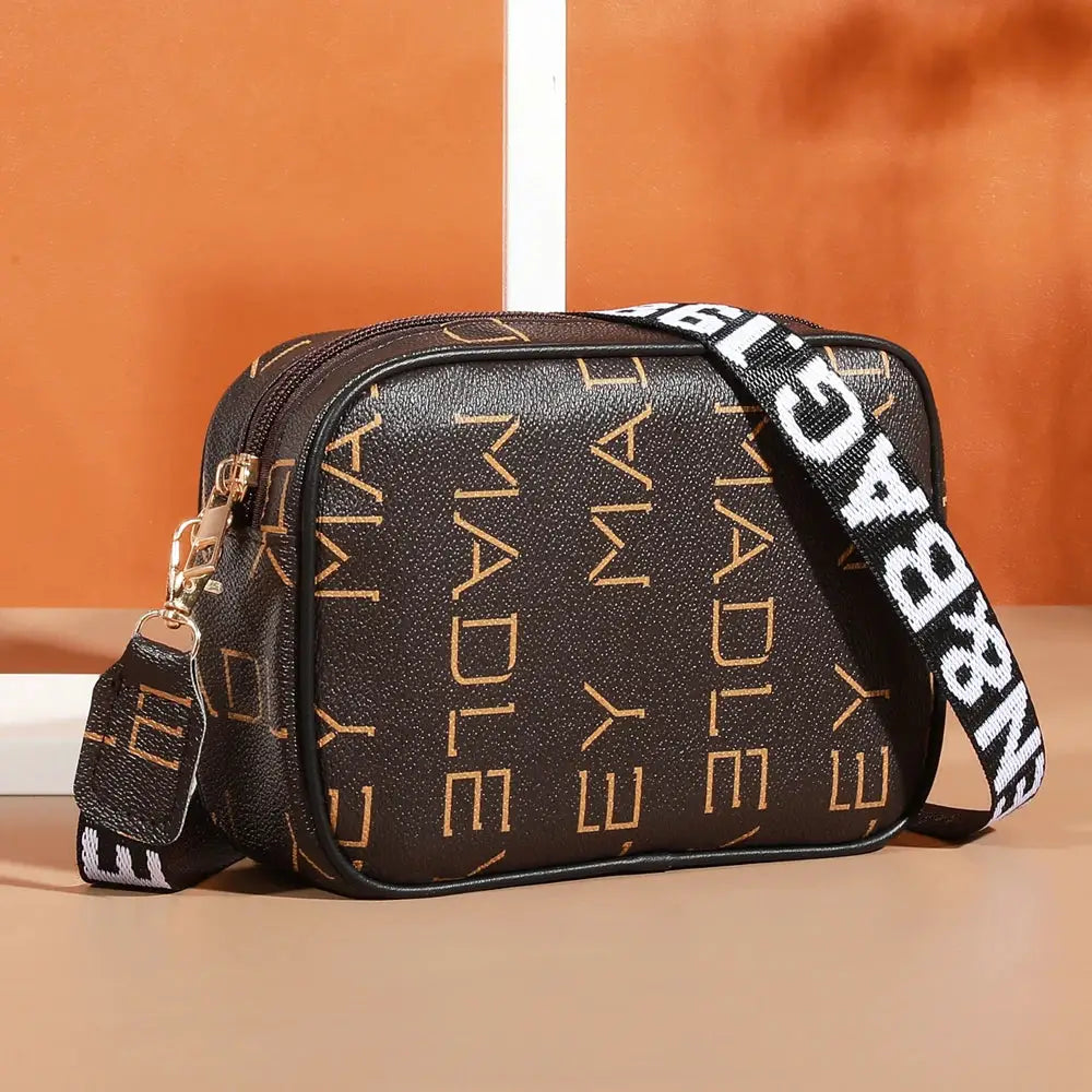 Simples Market crossbody bag; black textured faux leather with gold geometric motif, adjustable strap, compact daily bag.