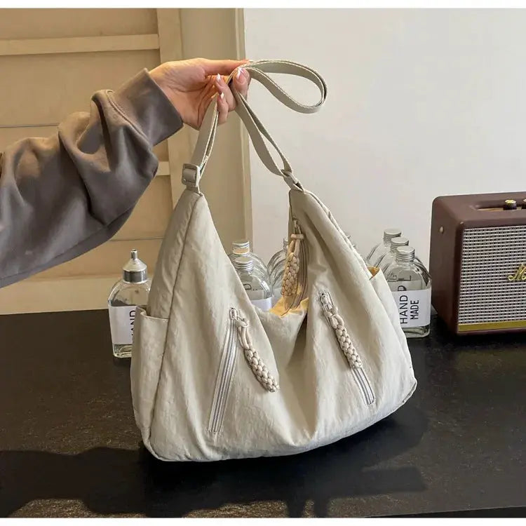 Soft gray cloth shoulder bag with braided zipper pulls, dual top handles, and front zip pockets