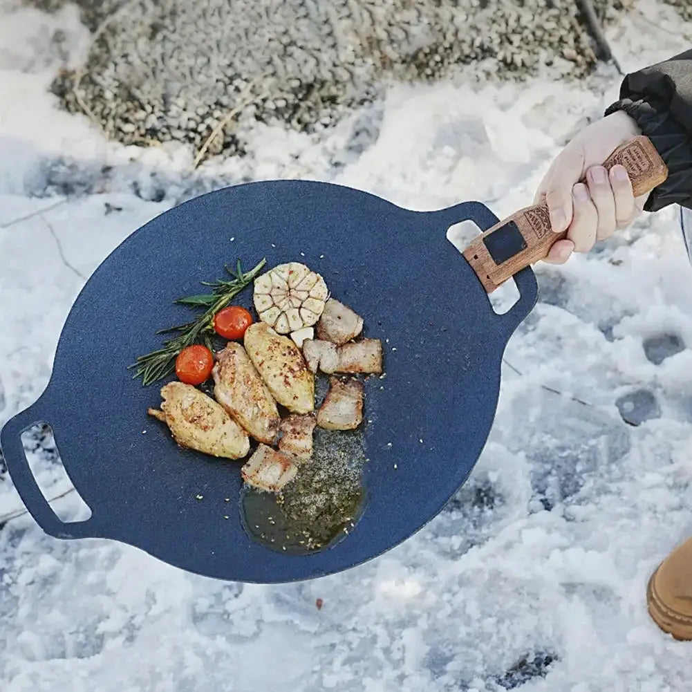Simples Market outdoor grill pan with solid wood insulated handle; blue pan cooking chicken and vegetables outdoors.