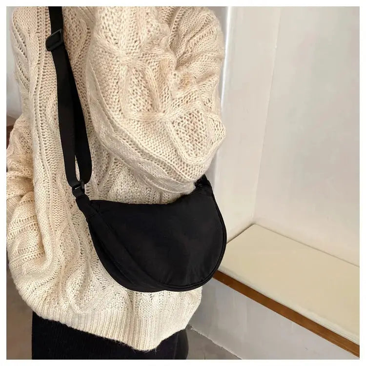 Casual nylon hobo crossbody bag in black with an adjustable strap, worn by a person in a cream knit sweater.