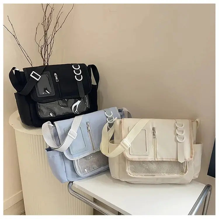 Three Ita bags in black, light blue, and cream with transparent front panels and crossbody straps.