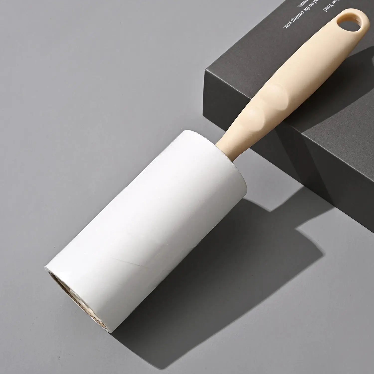 Lint roller with replaceable adhesive roll and beige wooden handle resting on a gray surface