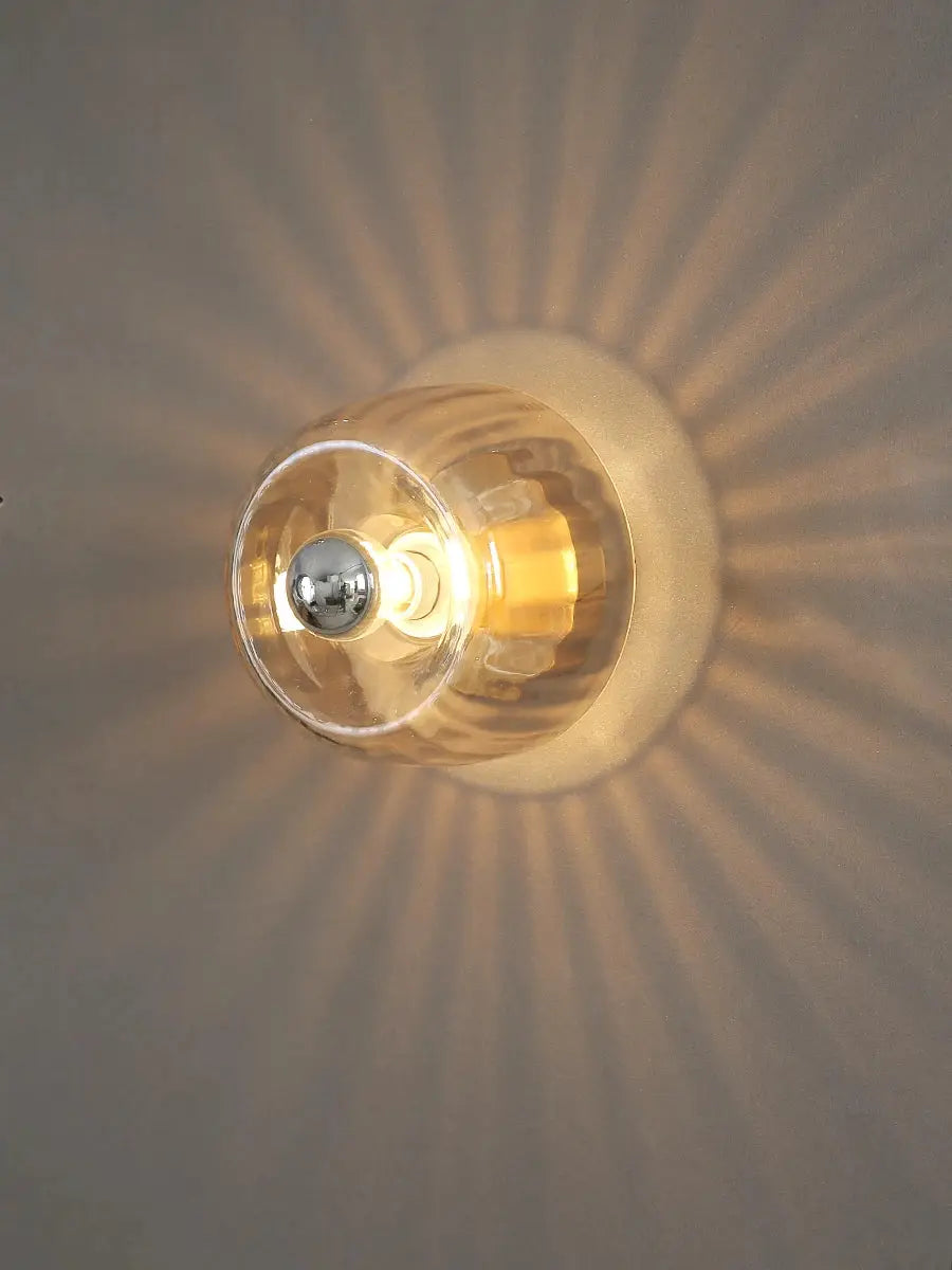 LED glass wall lamp with a clear globe and warm amber glow casting radial light on the wall.