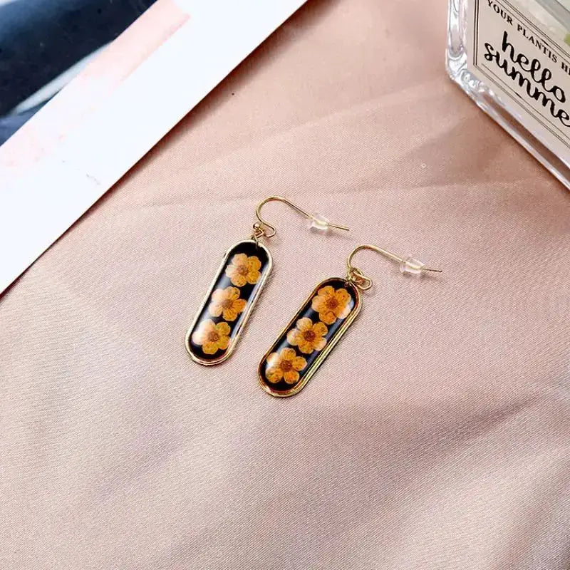 Pair of pressed flower epoxy resin earrings with gold-tone rectangular frames and fishhook backs, yellow blossoms inside