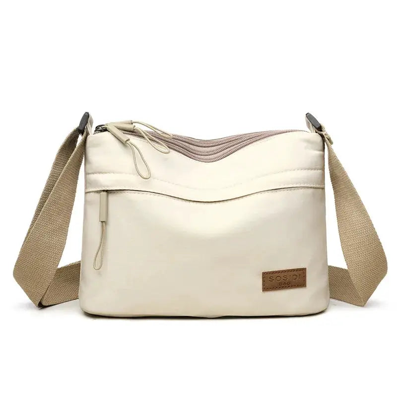 Cream canvas shoulder crossbody bag with beige strap and front zip pocket, 3 main pockets