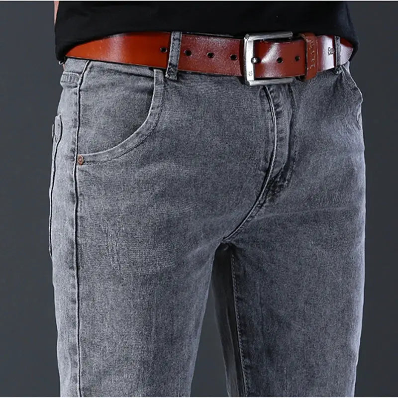Men's gray denim jeans with a brown leather belt, front pockets and rivet accents.