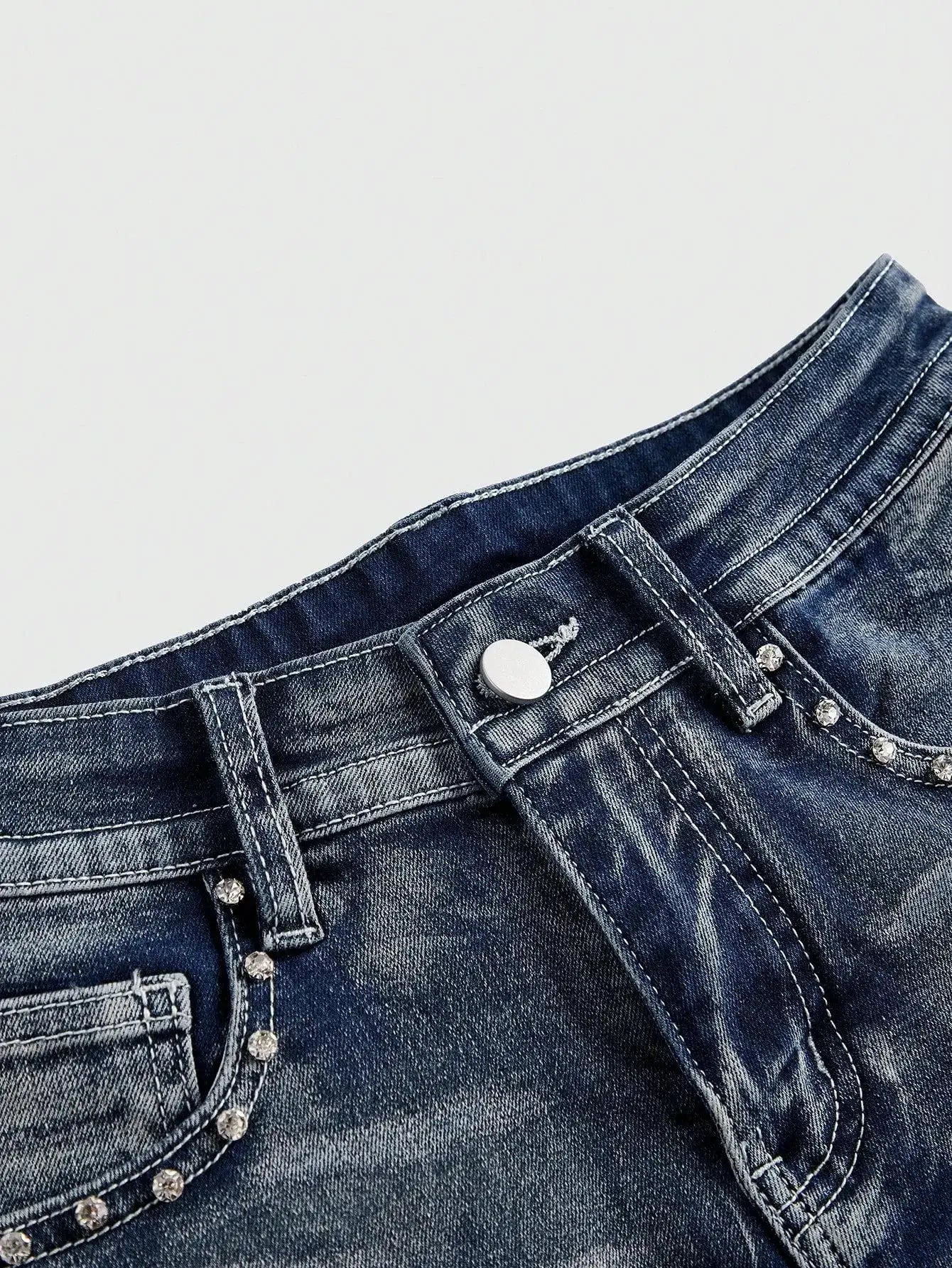 Low-rise distressed blue denim shorts with white stitching and metal stud embellishments on the pockets.