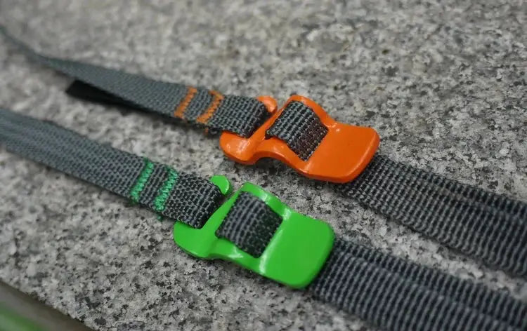 Two camping luggage straps with quick-release plastic buckles, orange and green, on gray webbing.