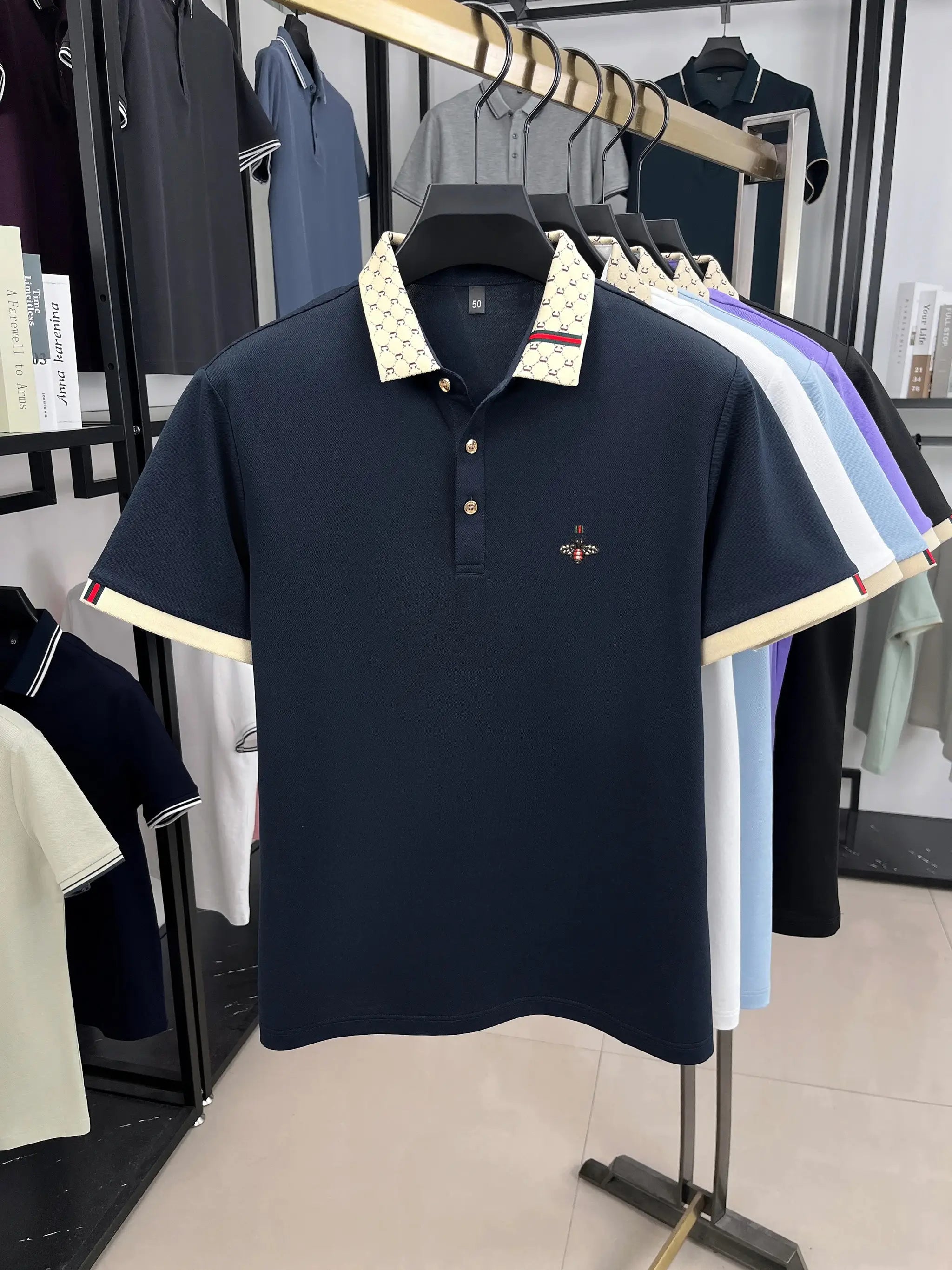 Navy polo shirt with beige patterned jacquard collar and bee embroidery on chest.