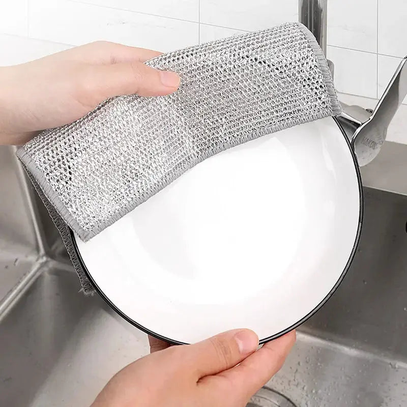 Steel wire dishcloth in silver used to wipe a white plate in the kitchen sink