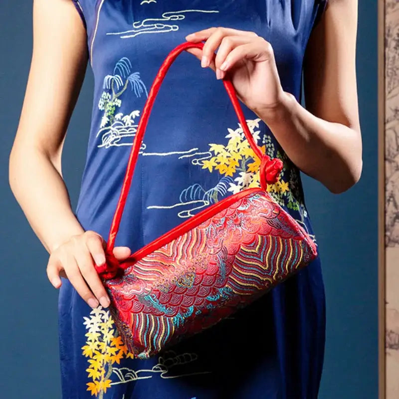 Shoulder bag with red satin trim and multicolor silk embroidery on a compact purse, held by a model.