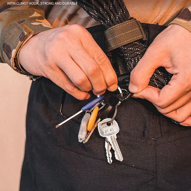 Outdoor tactical gear: hands attach carabiner and keys to a belt loop, with rope and camouflage clothing.
