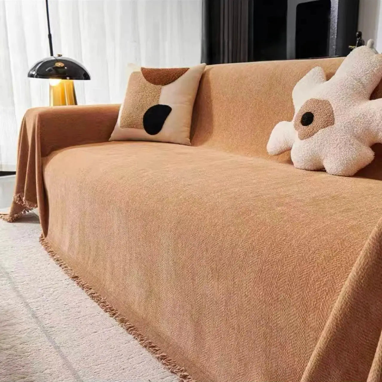 Camel chenille sofa cover with tassel edge, draped over a beige couch with decorative cushions and a plush star pillow.