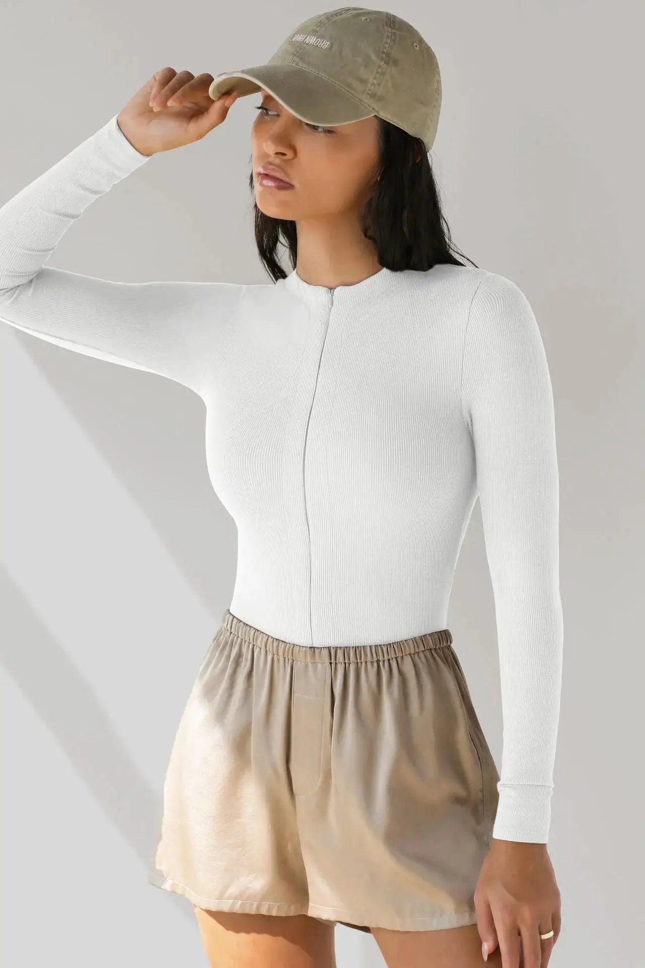Jumpsuit-style white ribbed knit top with front zipper, paired with beige satin shorts on model