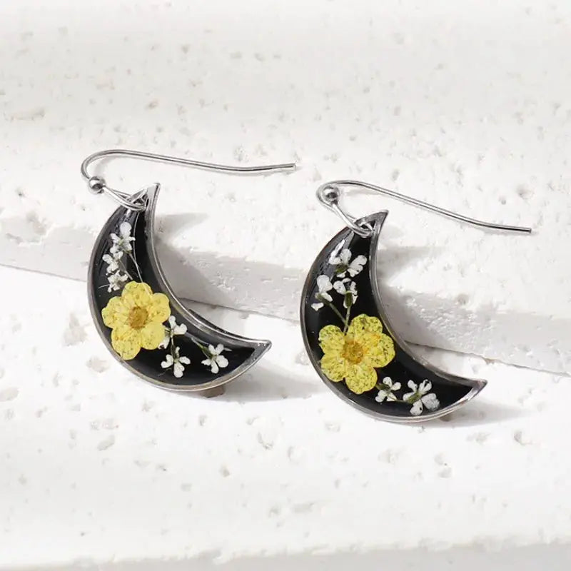 Simples Market pair of crescent moon earrings with pressed yellow flowers and white blossoms in black epoxy resin.
