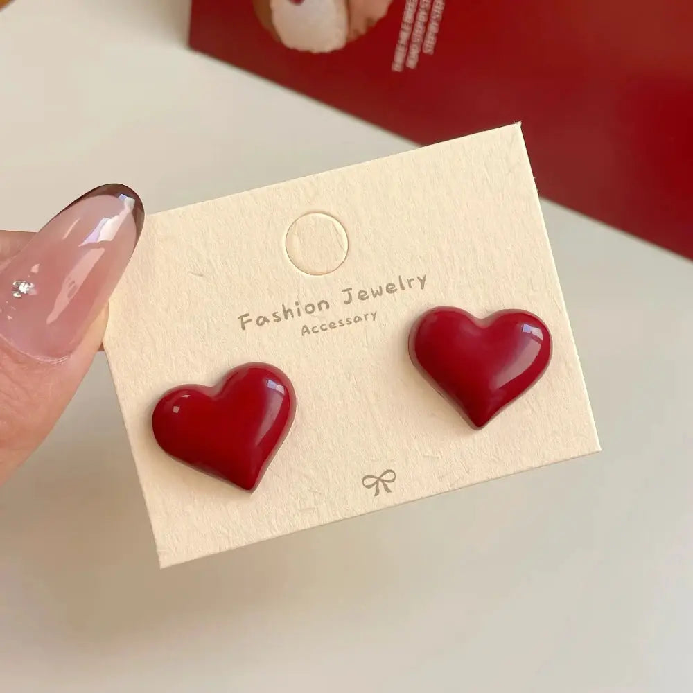 Pair of red enamel heart-shaped stud earrings on a beige fashion jewelry card
