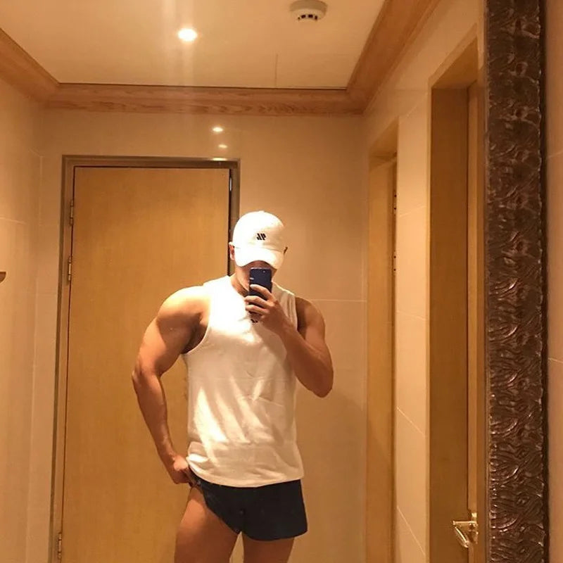 Mens white sleeveless bodybuilding tank top with black shorts and white cap, mirror selfie