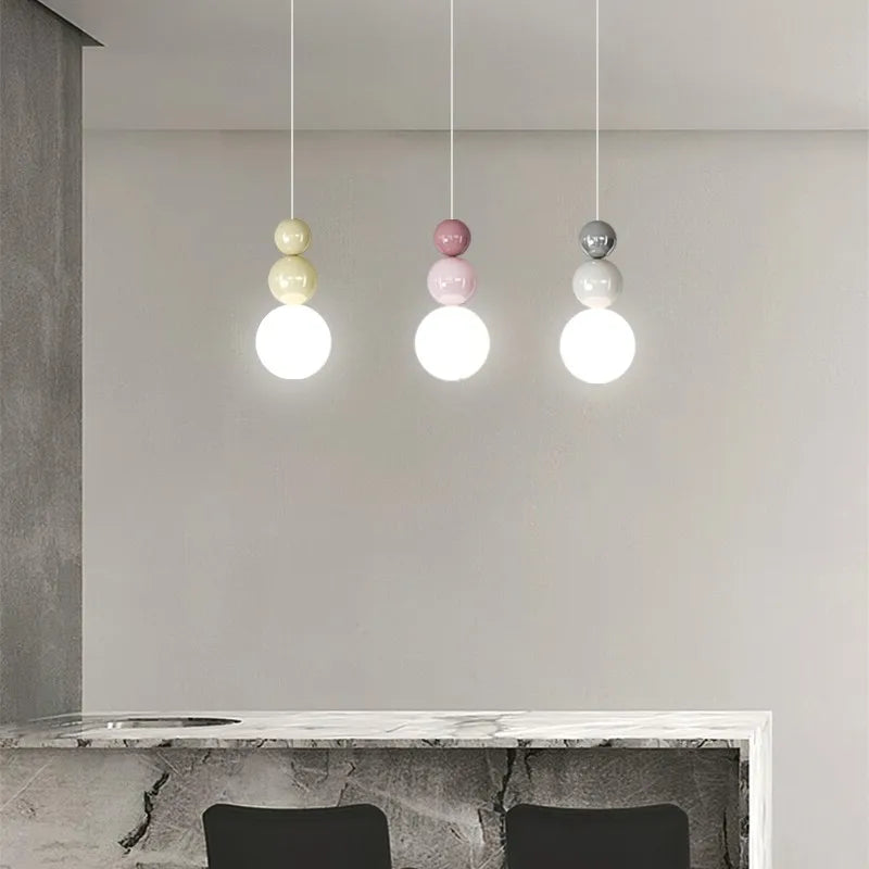 Nordic pendant lights, three pastel bead-top fixtures in cream, pink and gray with LED bulbs over a marble counter.