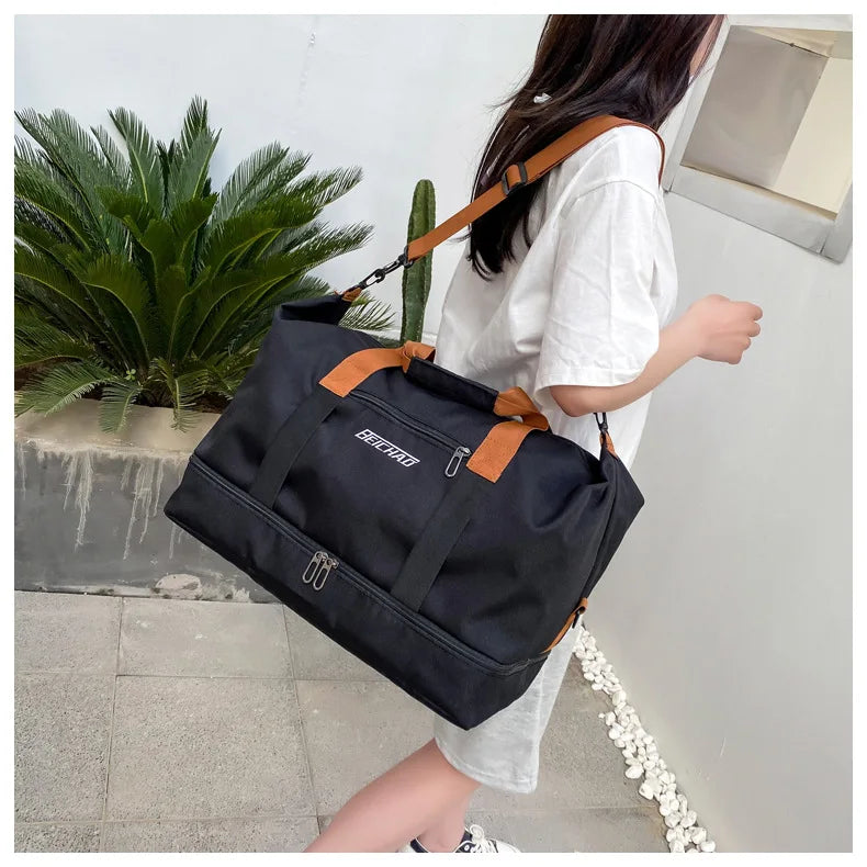 Large-capacity black travel gym bag with brown handles and strap carried by a person in a white t-shirt.