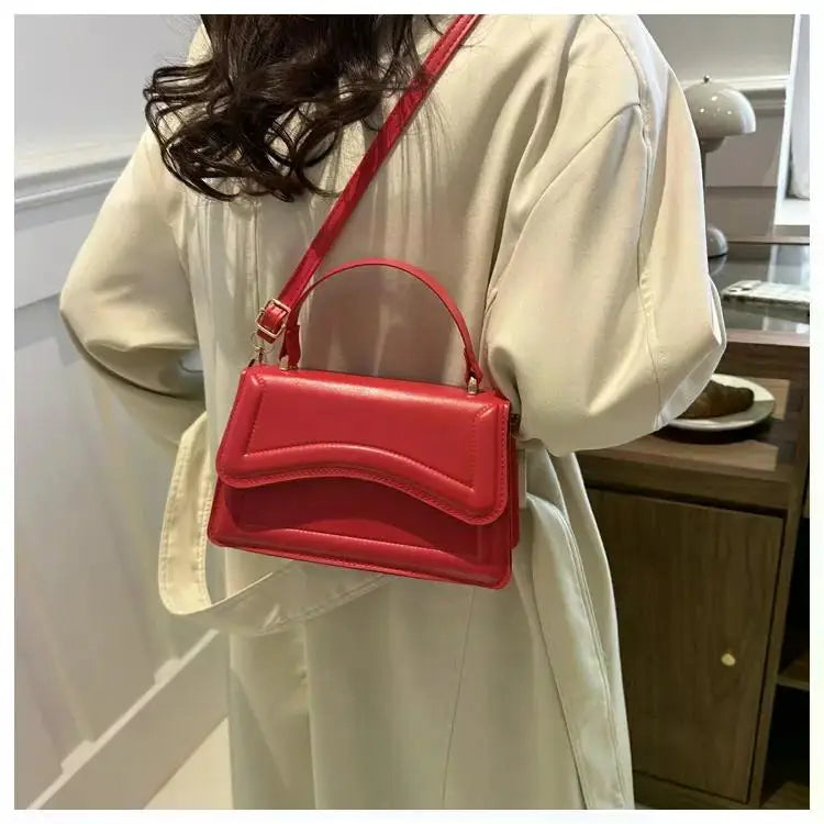 Small red PU leather handbag with curved flap and crossbody strap