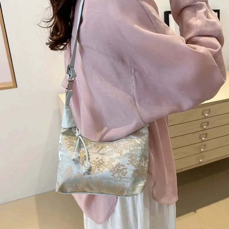 Crossbody handbag with light blue and gold floral brocade pattern and gray adjustable shoulder strap