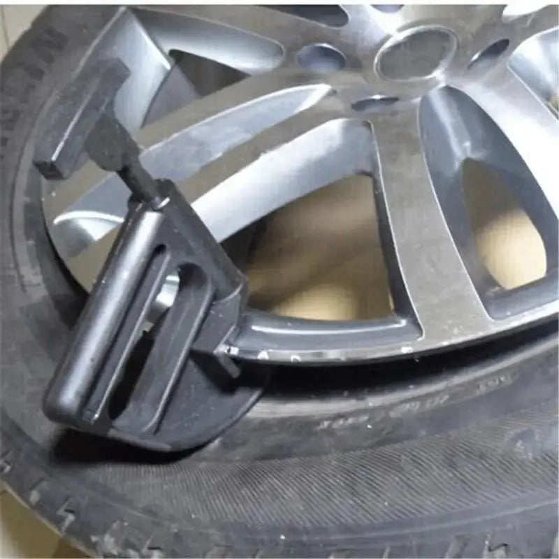 Automotive bead clamp tool for tire changing; black plastic clamp attached to a silver alloy rim and tire.