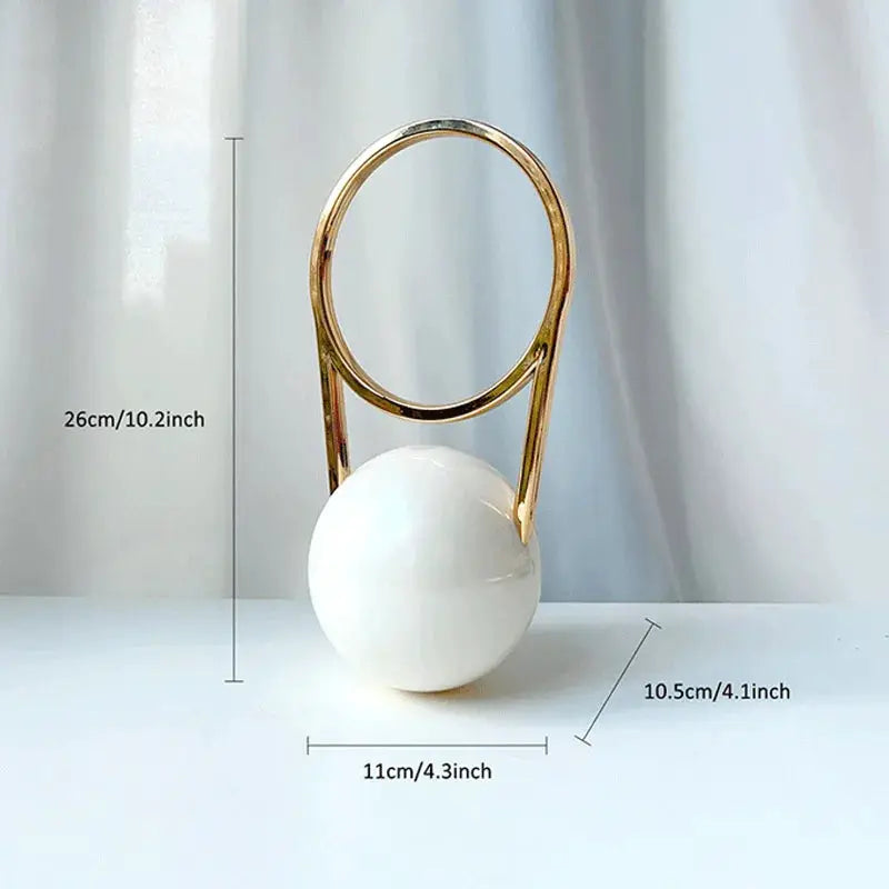 Luxury acrylic evening clutch by Simples Market with a gold circular ring handle atop a white marble ball base