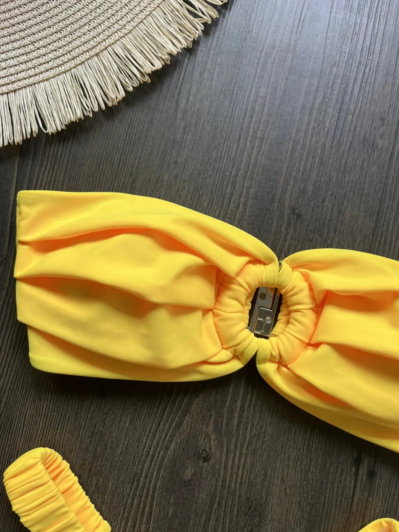 Bright yellow bandeau bikini top with knot center from Simples Market on dark wood background with fringe mat
