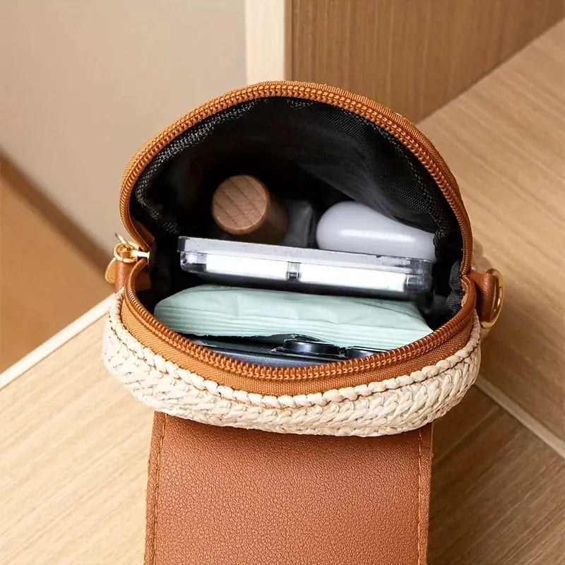 Mini crossbody phone bag, brown faux leather with woven straw trim, open to reveal compact and cosmetics.