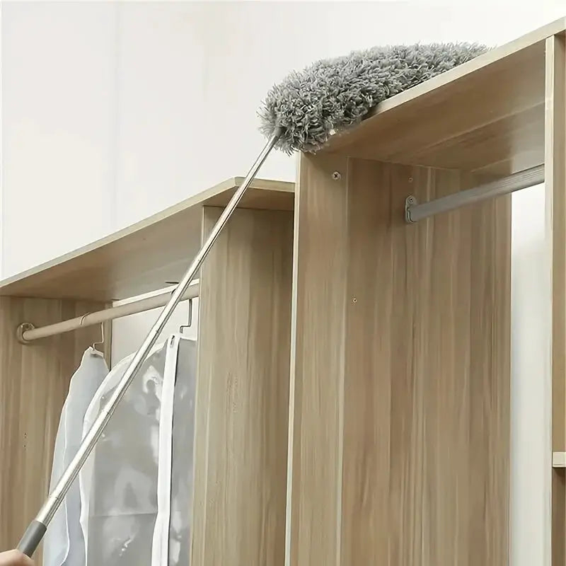 Cleaning duster with extendable metal handle and gray microfiber head dusting inside a wardrobe.
