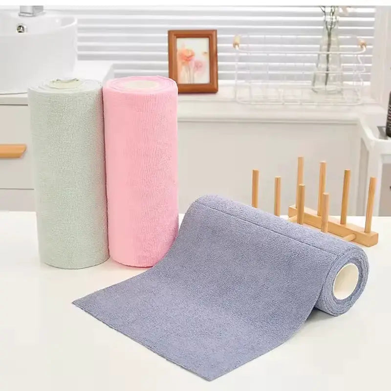 Three microfiber kitchen towel rolls in green, pink, and purple with one unrolled on a white counter.