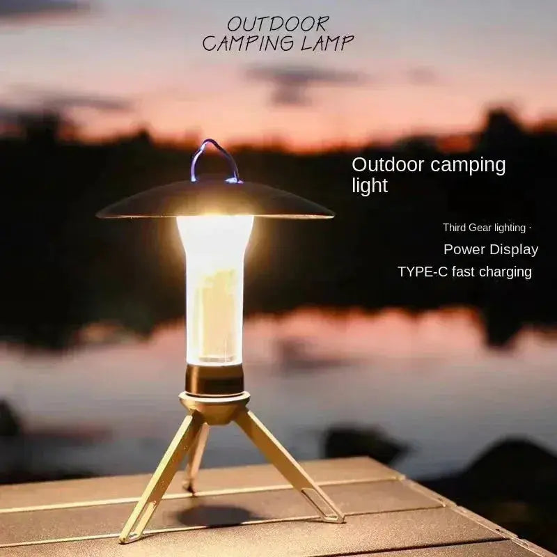 Portable camping lantern on a gold tripod with black shade, outdoor sunset backdrop
