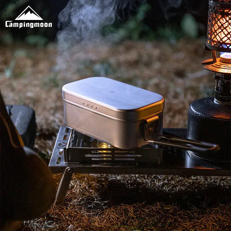 Aluminum lunch box by Simples Market on open-flame camping stove; silver metal with CampingMoon logo.
