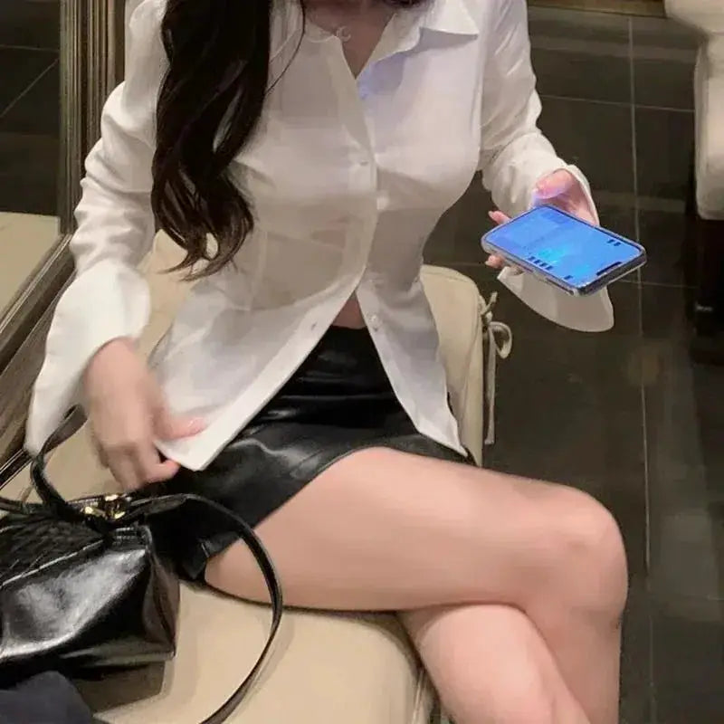 Women's white button-down blouse with lapel collar and long sleeves, paired with a black mini skirt.