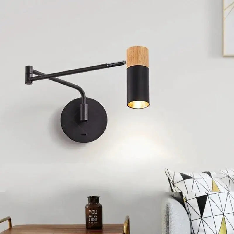 Modern black wall lamp with wood accent and adjustable cylindrical shade mounted on a circular base.