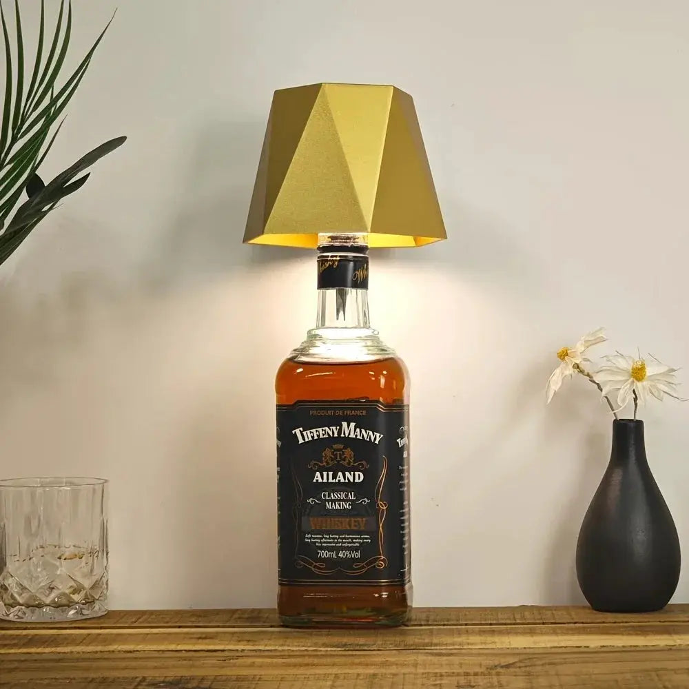 Lampe de table sans fil en forme de bouteille avec abat-jour doré, posée sur une bouteille de whisky; commande tactile