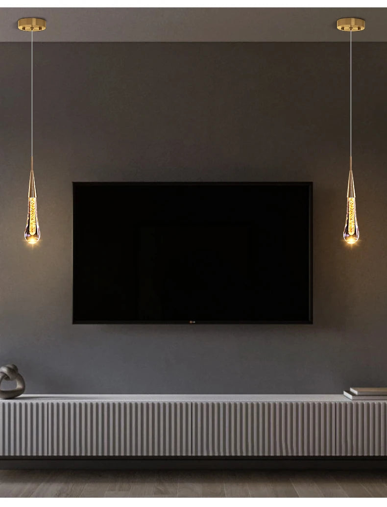 Two gold-tone crystal LED pendant lights hanging over a wall TV in a modern living room.