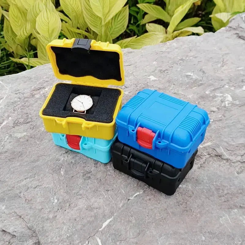 Four compact PP toolbox storage cases in yellow, turquoise, blue and black; yellow case open with foam insert and a watch.