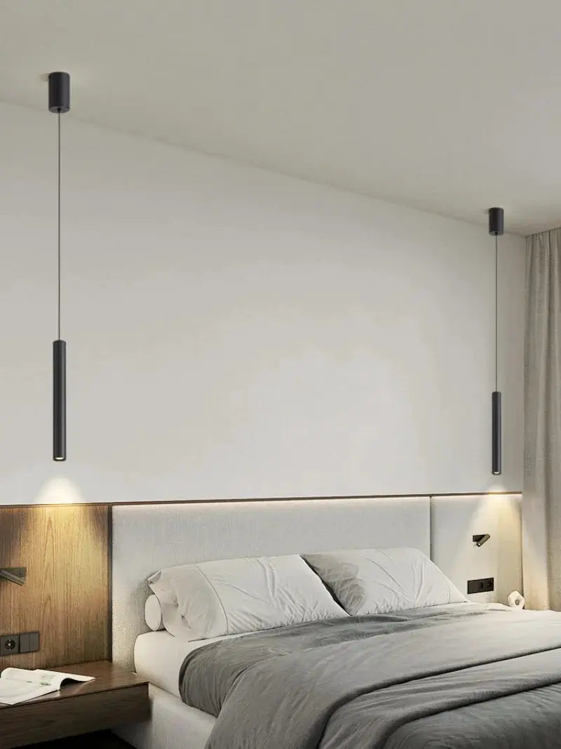 Pair of minimalist bedside pendant lamps, black cylindrical, hanging over a bed in a modern bedroom