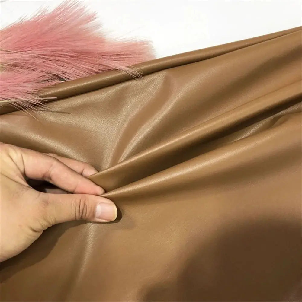 Women's PU leather skirt fabric swatch in tan-brown faux leather; close-up of glossy material being held.