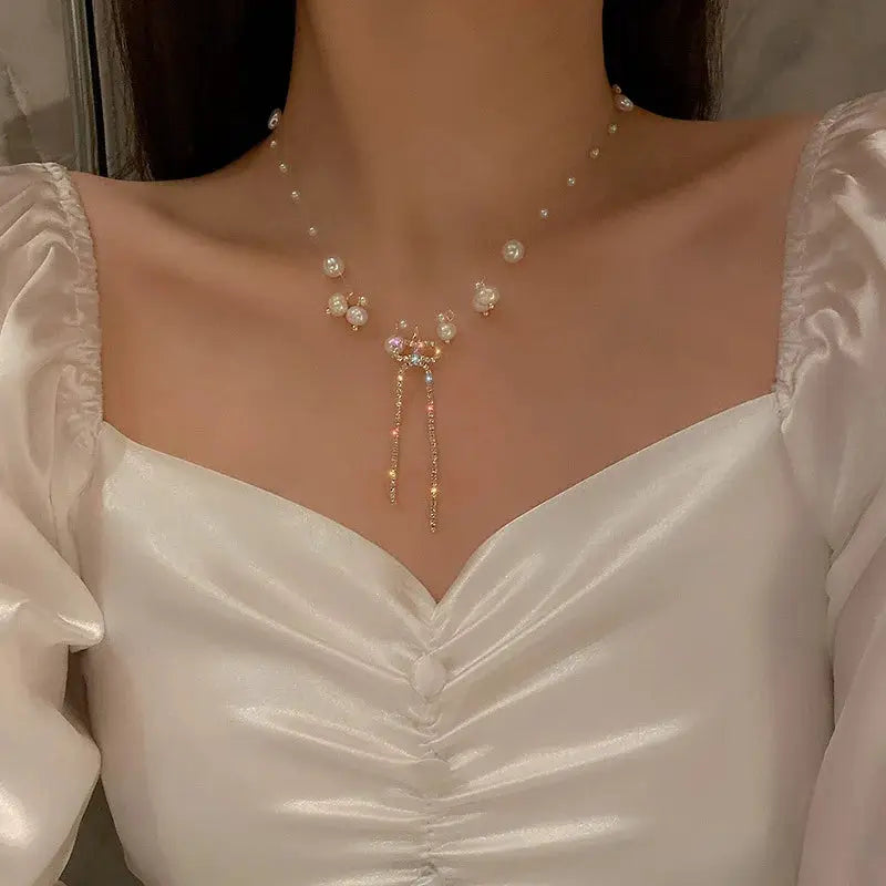 Pearl choker necklace with gold-tone pendant and tassel strands on a model wearing a white satin top.