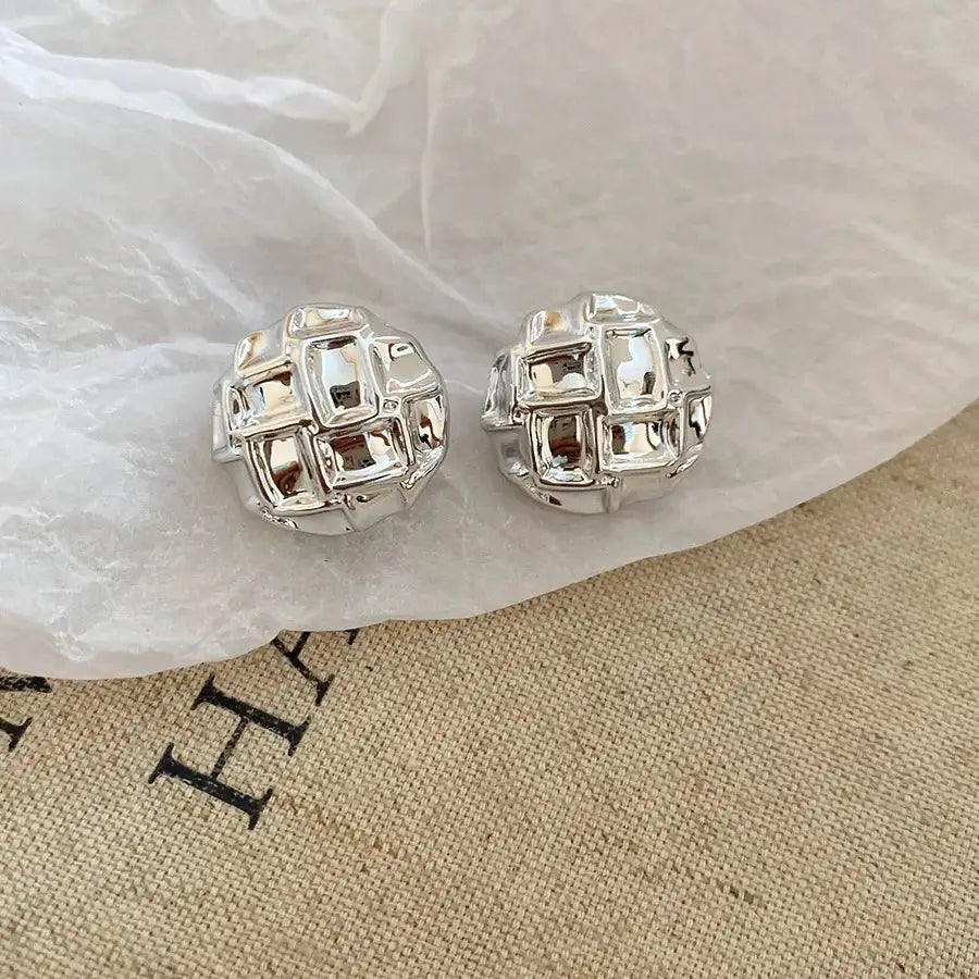 Silver-toned acrylic stud earrings with irregular pleated oval shape and geometric square lattice by Simples Market