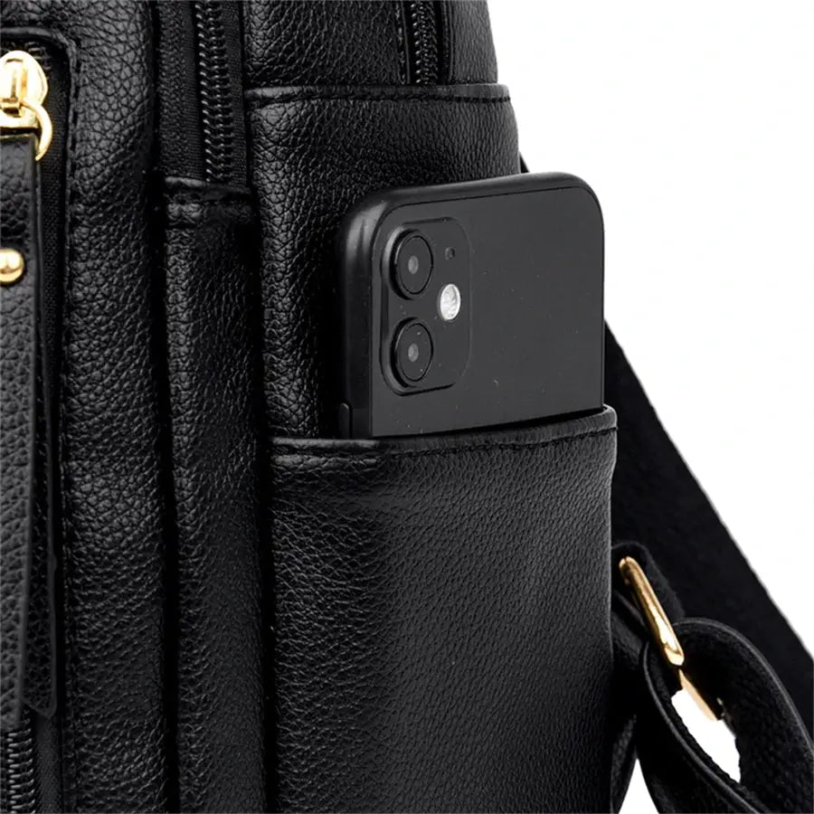 Black leather backpack with side pocket holding a smartphone and gold-tone hardware