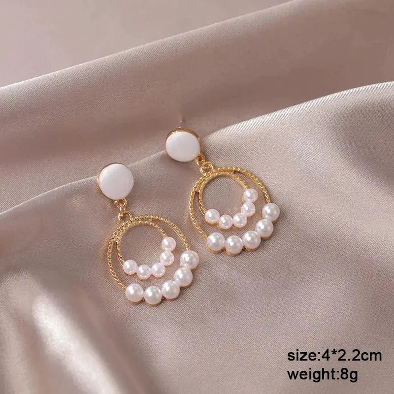 Pair of white dangle earrings with gold-tone circular hoops and pearl arc embellishments, round enamel studs