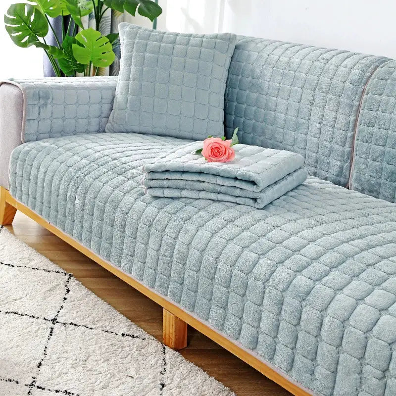 Flannel sofa cushion set in light blue with quilted non-slip covers on a wooden sofa, folded throw and rose on top